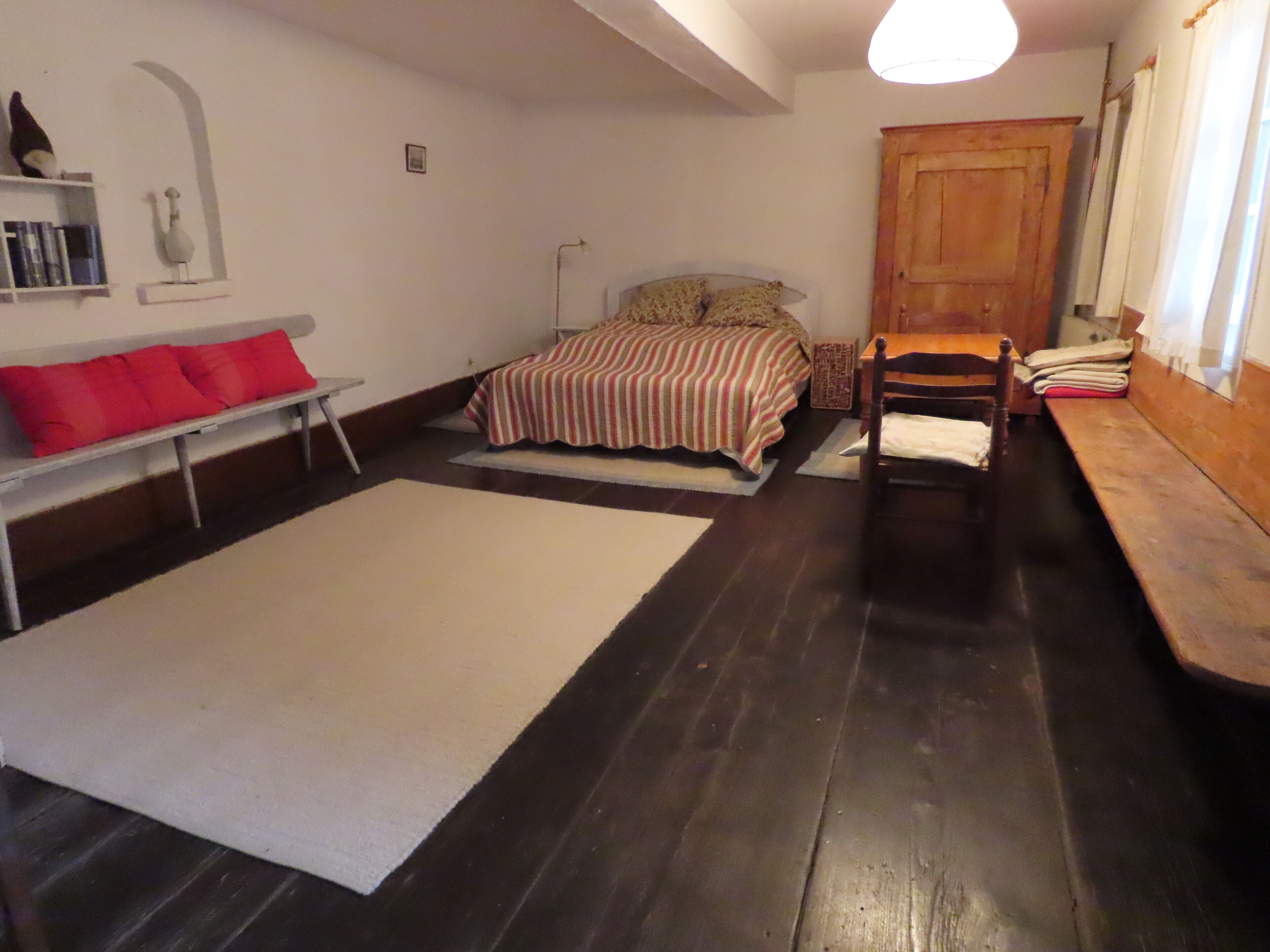 Une chambre à coucher avec un lit, un banc en bois, une petite table et un mur blanc avec une étagère.