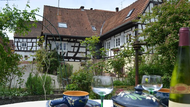 A traditional half-timbered house with a tiled roof, surrounded by greenery and a table with a wine bottle and glasses. - Idyllic half-timbered house with a large garden and playground and orchard (Cleebourg)