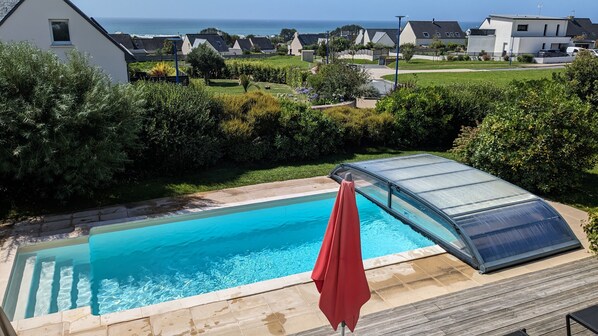A swimming pool with a glass enclosure, surrounded by a wooden deck and a red umbrella.