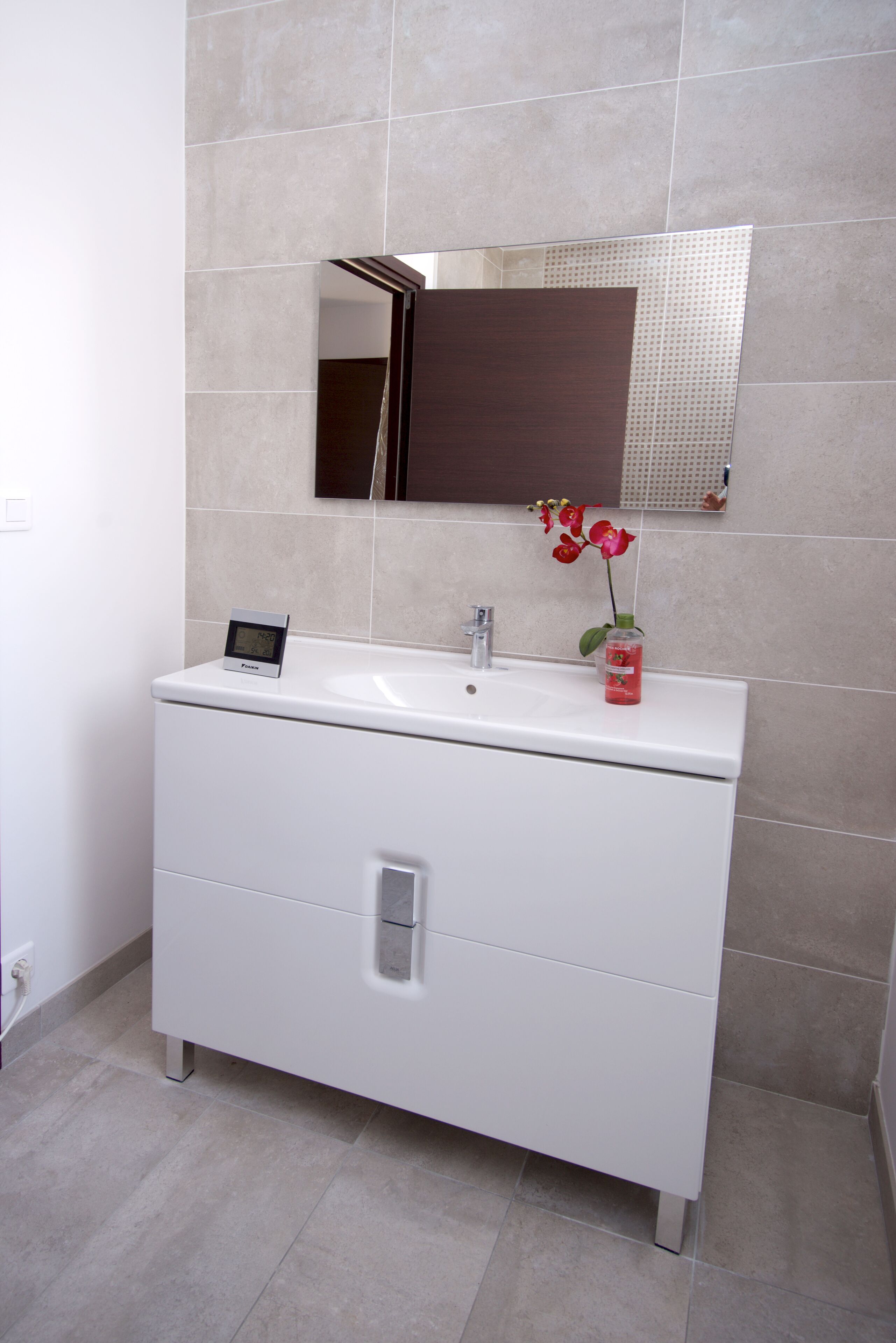 A modern bathroom with a white vanity, a mirror, and a small flower arrangement.