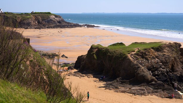 Uma praia costeira com afloramentos rochosos e vista clara do oceano.