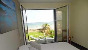 Un dormitorio con una cama grande, vistas a la playa y una silla junto a la ventana.