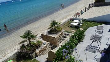 Une plage à l’eau d’un bleu cristallin, un sentier de pierres menant à un patio doté de sièges extérieurs, et une vue sur la mer.