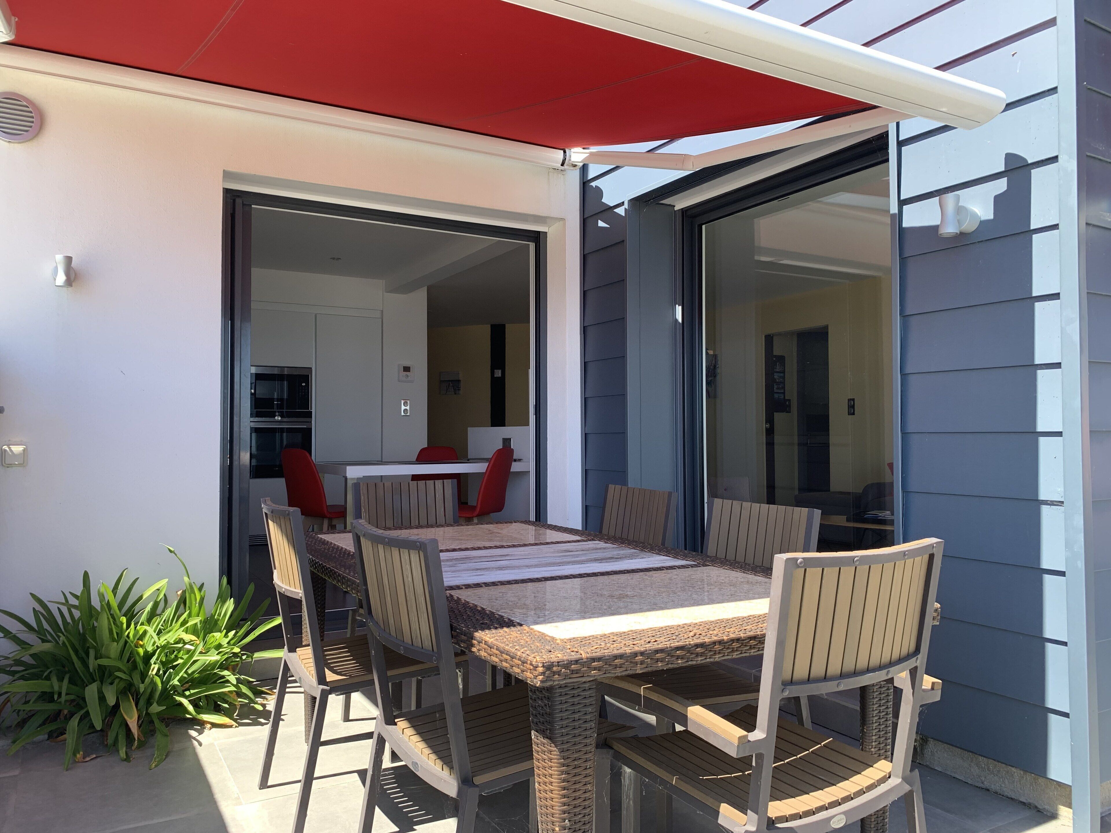 An outdoor patio with a dining table and chairs, a red awning, and a sliding glass door leading to an interior space.