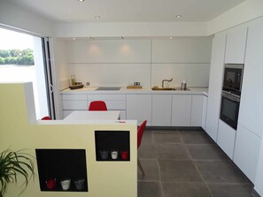 Une cuisine moderne avec des meubles blancs, une chaise rouge, un évier et un four.