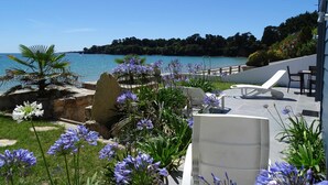 Un patio con mobiliario exterior, vista al mar y un jardín con flores moradas.
