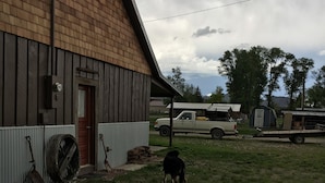 Un granero rústico con fachada de madera, un camión estacionado afuera y un perro al fondo.