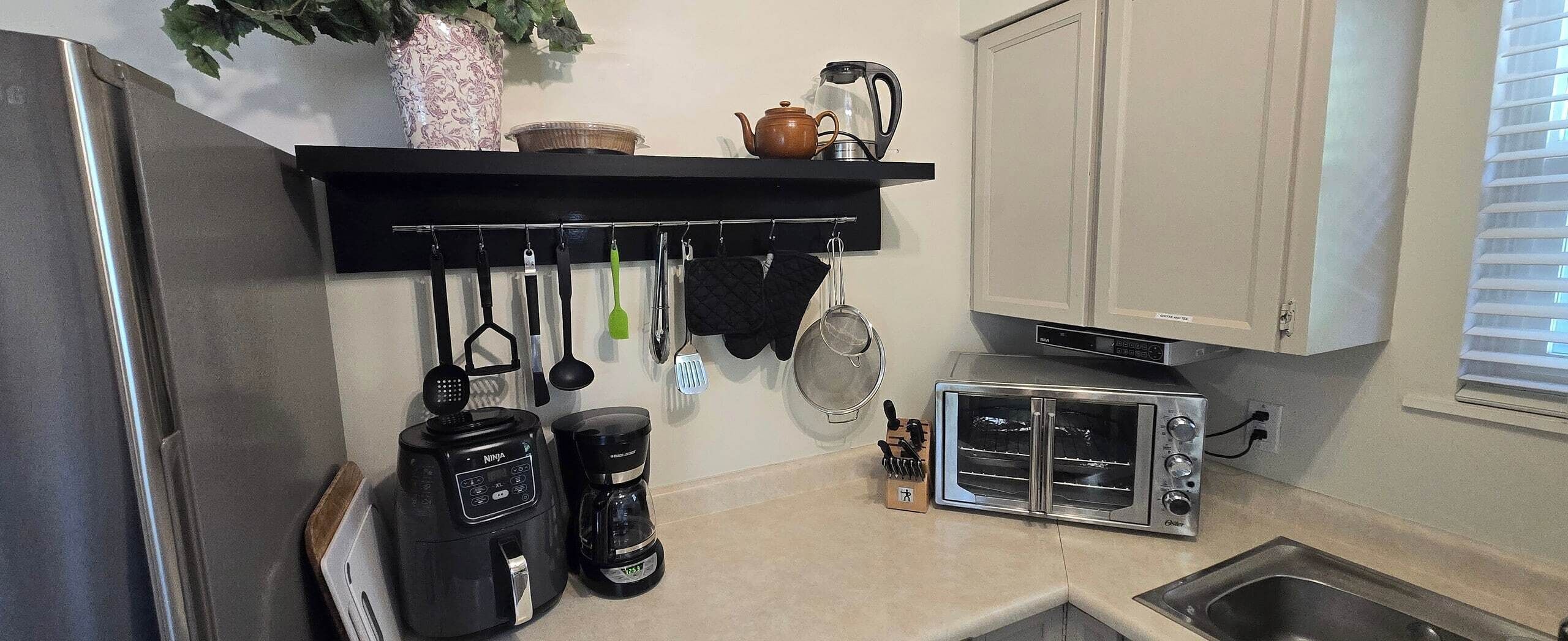 A kitchen with a toaster oven, a coffee maker, and a hanging utensil rack.