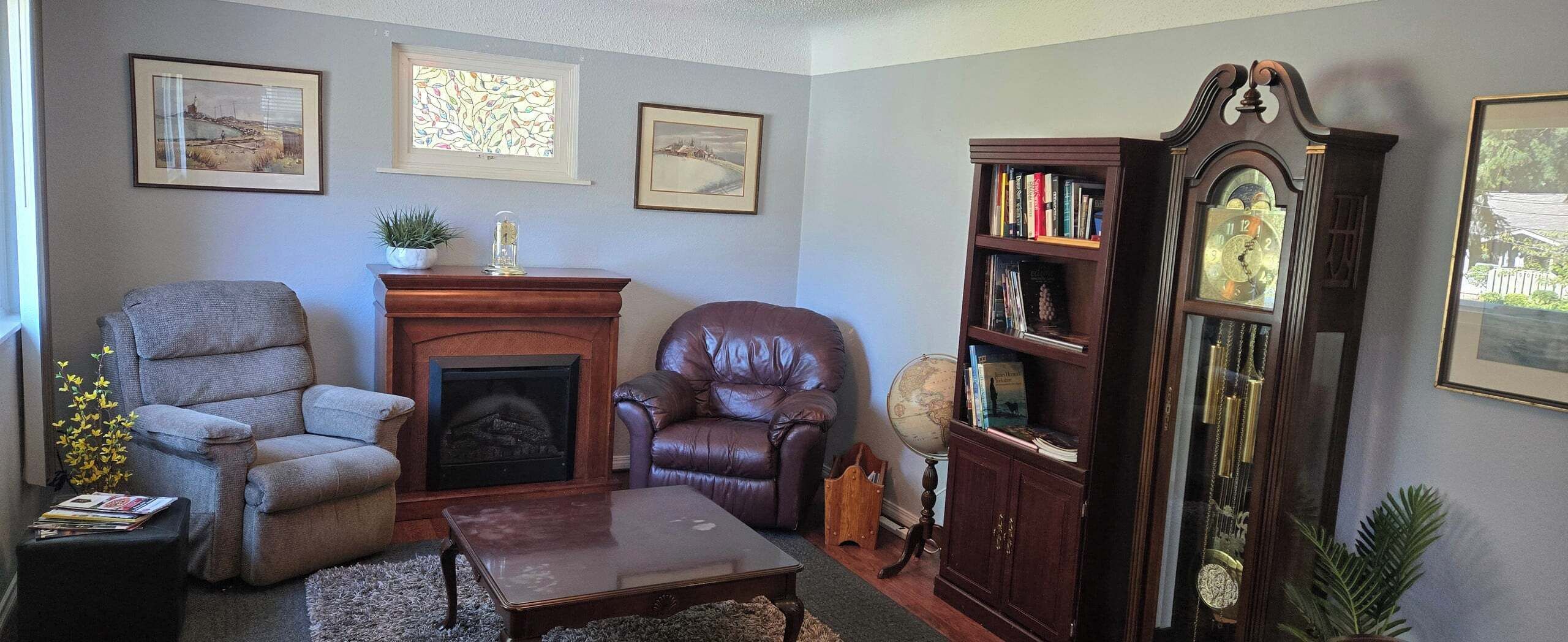A living room with a fireplace, leather chairs, a coffee table, a bookshelf, and a grandfather clock.