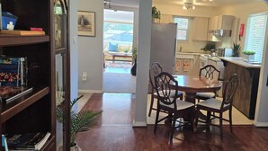 Un comedor con una mesa y sillas de madera, una cocina al fondo y una estantería llena de libros.