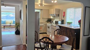 A kitchen with white cabinets, a dining table with chairs, and a window with blinds. - The Suite Spot is a lovely two bedroom suite in a quiet neighborhood (Victoria)