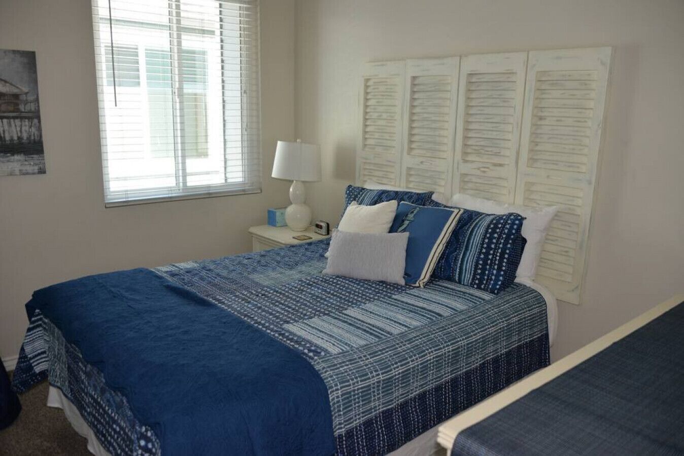 A bedroom with a large bed, a bedside table with a lamp, a window with blinds, and a wall with papers.