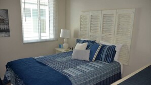 Une chambre à coucher avec un grand lit, une table de chevet avec une lampe, une fenêtre avec des stores et un mur recouvert de papiers.