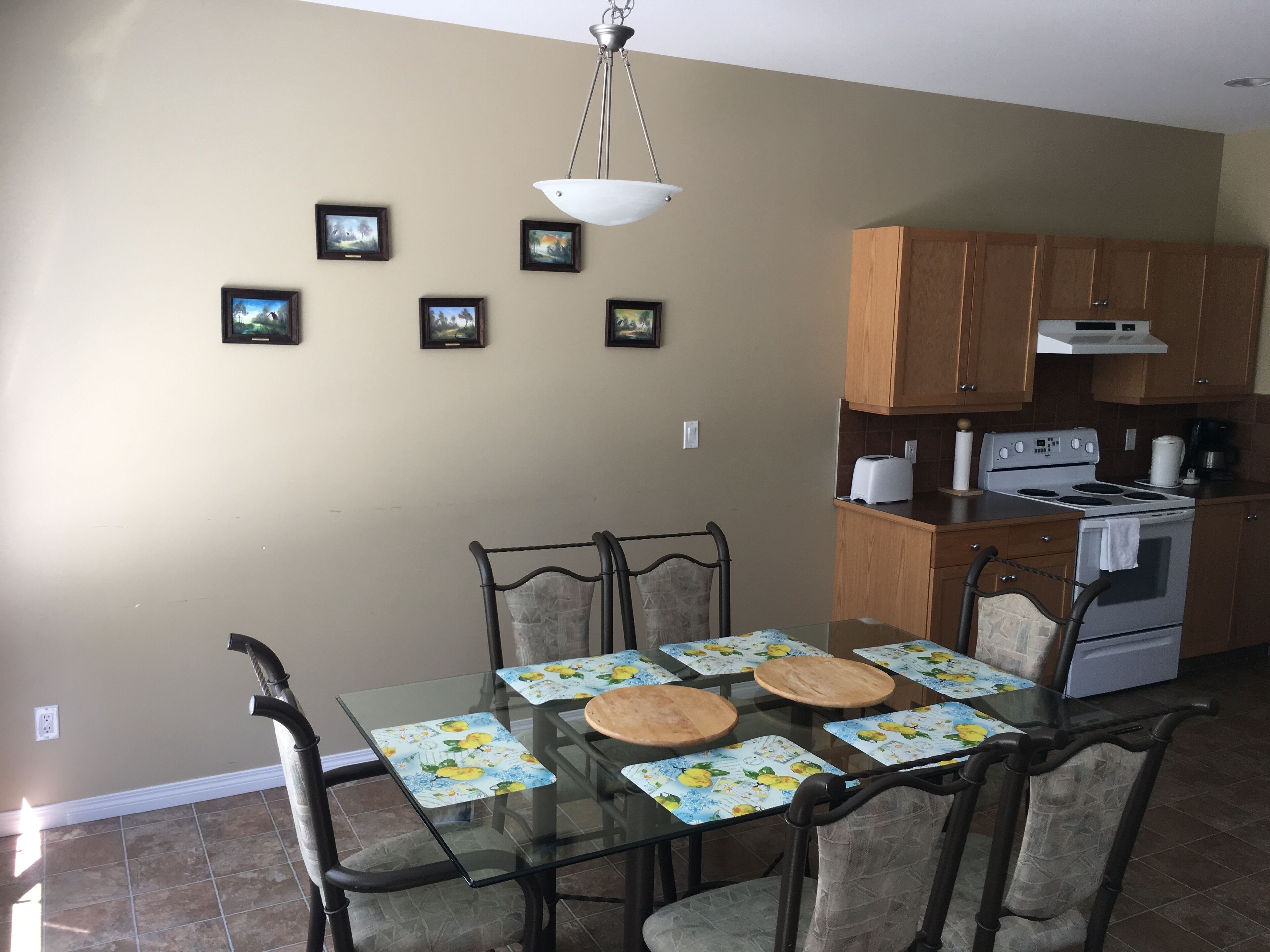 Un comedor con mesa de vidrio, sillas y una cocina al fondo.