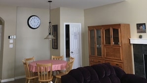 Uma sala ampla com uma mesa de jantar, cadeiras, um sofá roxo, um armário de madeira e um relógio na parede.