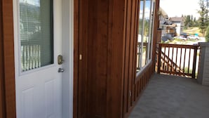 Uma porta de madeira com janela, um alpendre com balaústres de madeira, e vista para uma rua residencial.