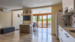 Una cuina moderna amb forn integrat, zona de menjador amb taula i cadires, i una gran porta corredissa de vidre que dona a un pati exterior.