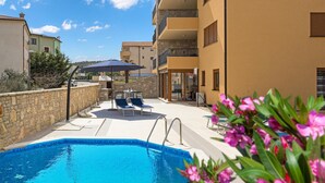Una piscina amb gandules i ombrel·les, un mur de pedra i un edifici amb balcons.