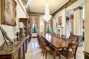 Une salle à manger élégante, avec une longue table en bois, des chaises, des lustres et un décor classique.