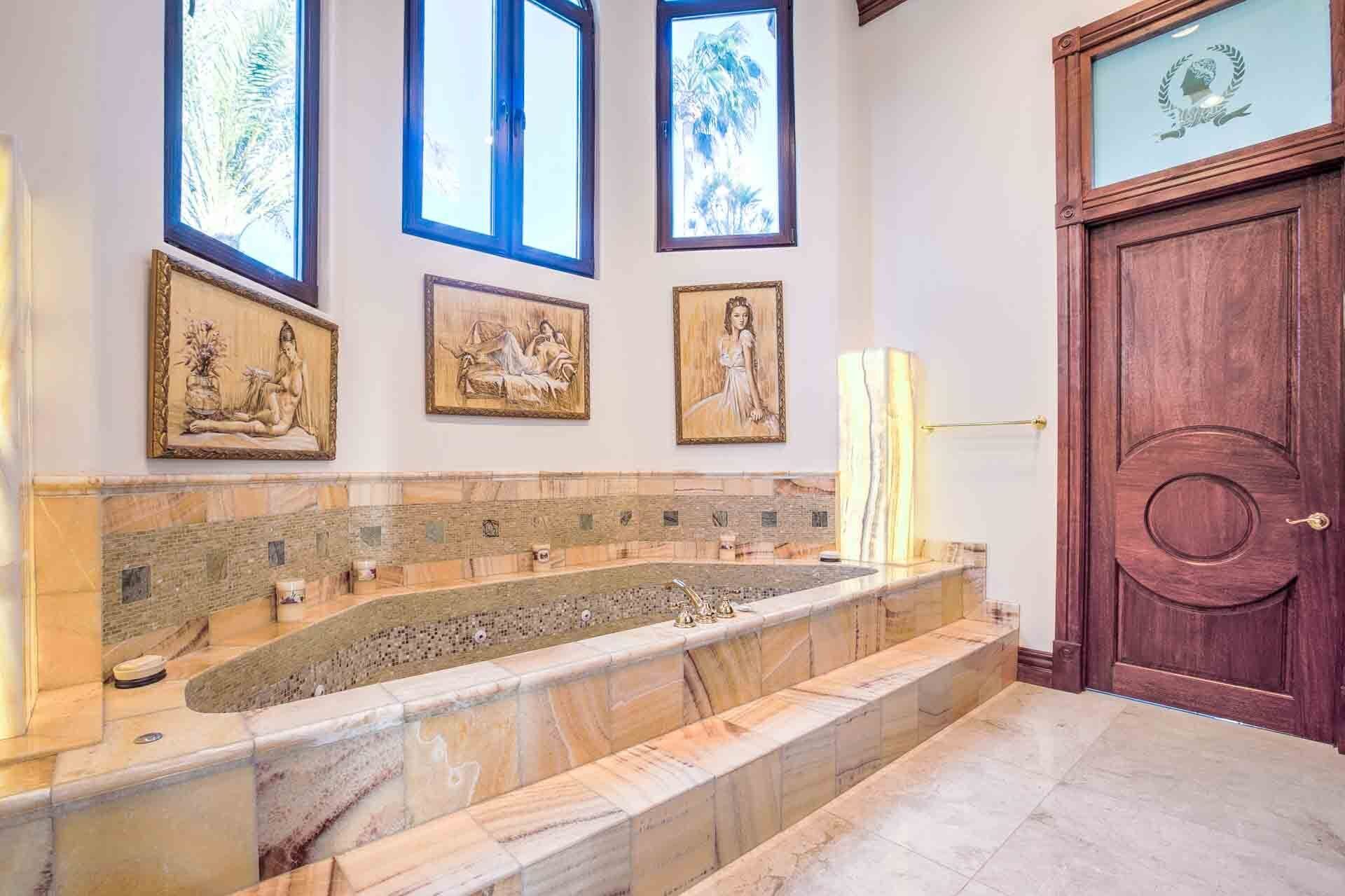 Une salle de bain avec une baignoire en marbre, des œuvres d’art encadrées au mur et une porte en bois.
