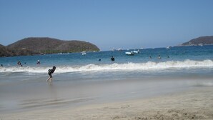 A beach with clear skies, calm waters, and boats in the distance. - Beautiful Pool Side Condo, Ground Level.  Close to Beach & Town Center   (zihuatanejo)