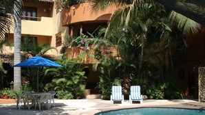 A pool area with lounge chairs, a table, and a blue umbrella. - Beautiful Pool Side Condo, Ground Level.  Close to Beach & Town Center   (zihuatanejo)