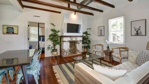 A living room with a glass coffee table, a sofa, and a fireplace. There are chairs and a dining table in the background. - Perfect 2bd Suite w. Porch, Near King Street! (Charleston)