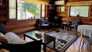 A cozy cabin interior with wooden walls, a sofa, a table, and a TV. - Rustic Waterfront Log Cabin (Kaslo)