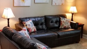 Un salon avec un canapé en cuir foncé, deux tables d’appoint avec des lampes et trois tableaux aux motifs floraux accrochés au mur.