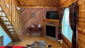 Un interior de madera con chimenea, un televisor sobre una repisa y una escalera.