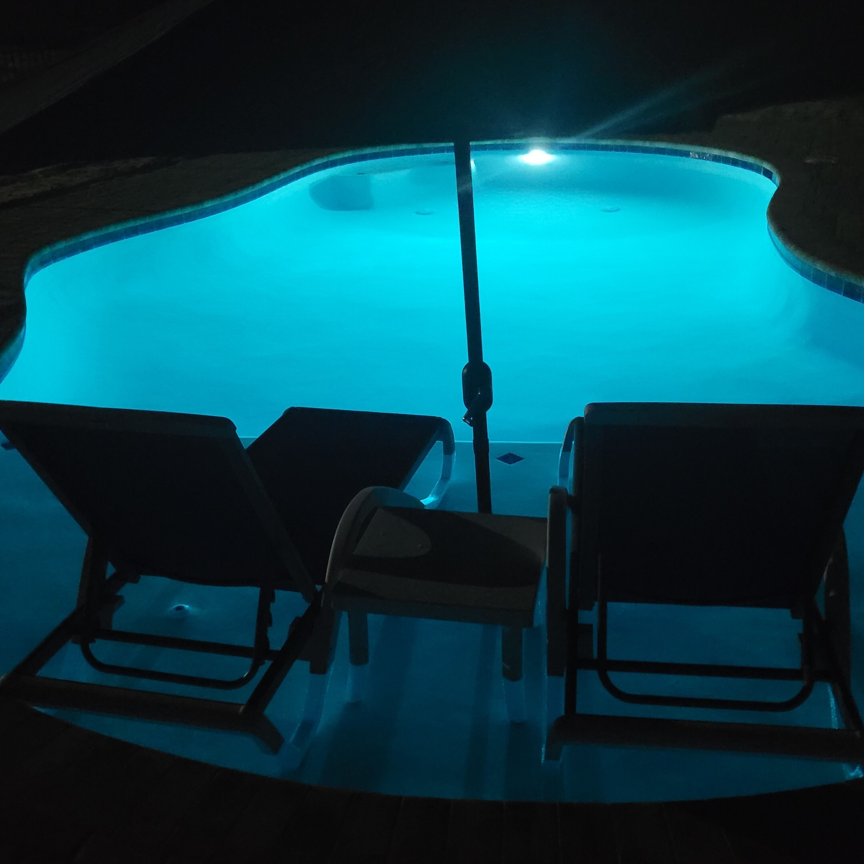 Une piscine avec deux chaises longues et une table, le tout entouré d’un petit muret.
