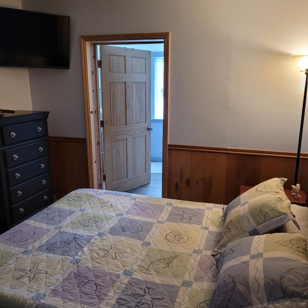 A bedroom with a bed, dresser, and a door leading to another room.