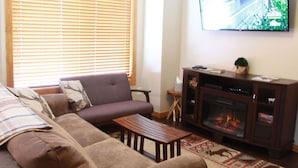 Una sala de estar con sofá, mesa de centro, chimenea y televisor montado en la pared.