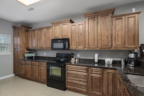 Modern kitchen with wooden cabinetry and sleek countertops, equipped with a refrigerator, oven, and microwave.