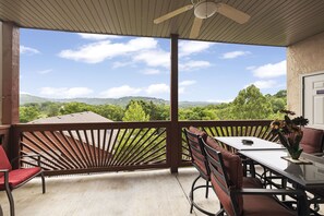 Enjoy the serene view of lush greenery from this balcony with a table and chairs.