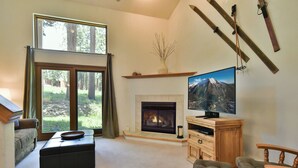 Ein Wohnzimmer mit Kamin, Fernseher und einem großen Fenster mit Blick auf einen Wald.