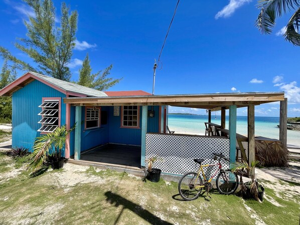 A small, single-story building with a porch overlooking a beach.