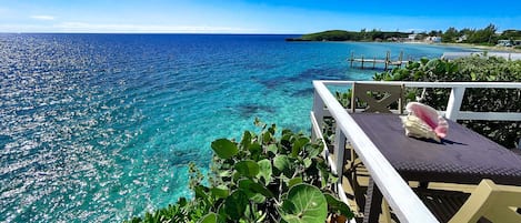 Vista despejada de un océano turquesa desde una terraza de madera con barandilla blanca, que da al mar hacia una pequeña isla con edificios y un muelle.