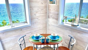 A corner room with a wooden floor, a table with blue plates, and chairs. - Ranked by VRBO/HomeAway Top 10 Most Unique Rentals Worldwide, Walk to Town. (Hatchet Bay, Eleuthera, Bahamas)