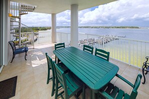 Un balcon avec une table et des chaises vertes, donnant sur une marina où sont amarrés des bateaux.