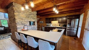 A modern kitchen with a large island, bar stools, a stone accent wall, wooden ceiling beams, and stainless steel appliances. - Spacious 4B-3B cabin-Stunning Views-Beautiful outdoor areas-By Fall Creek Falls (Spencer)