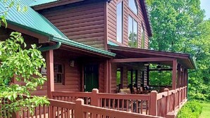 A two-story wooden cabin with a green roof, a porch with a railing, and a small deck area. - Spacious 4B-3B cabin-Stunning Views-Beautiful outdoor areas-By Fall Creek Falls (Spencer)