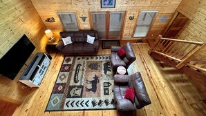A cozy cabin interior with wooden walls, a large window, a fireplace, and a sofa with decorative pillows. - Spacious 4B-3B cabin-Stunning Views-Beautiful outdoor areas-By Fall Creek Falls (Spencer)