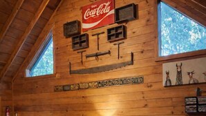 Ein gemütliches Blockhaus-Interieur mit einer Ledersofa, einem Coca-Cola Schild und rustikalen Dekorationselementen.