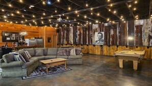 Ein gemütlicher Wohnbereich mit einer Couch, einem Couchtisch und einem Billardtisch, mit rustikalen Holzwänden und Lichterketten.