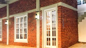 A brick building with three white-framed windows and a light fixture above each window. - No17 Residence (Kandy)