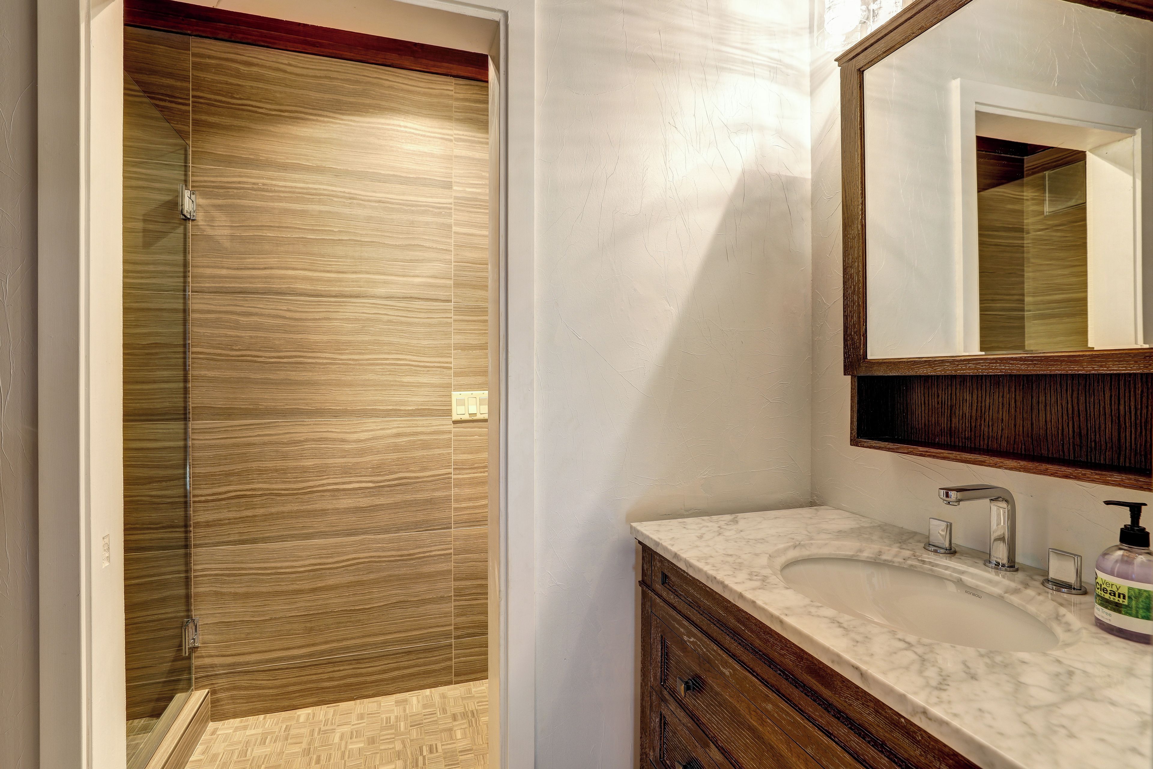 Un baño con cabina de ducha de madera, lavamanos de mármol y un espejo grande.