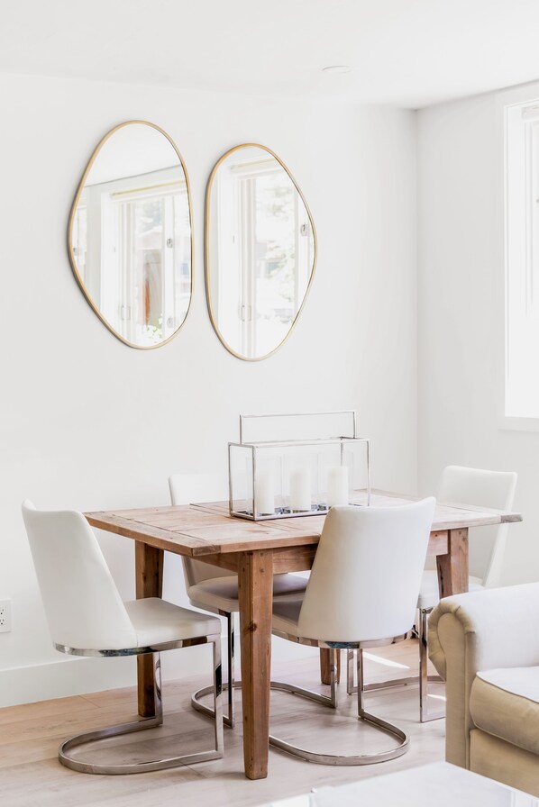 A dining area with a wooden table, white chairs, and two gold-framed mirrors on the wall.