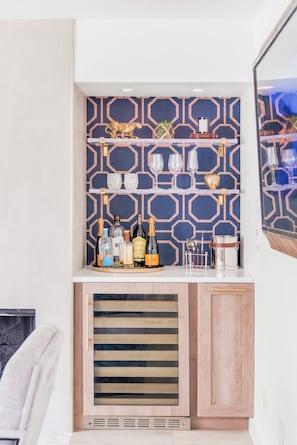 Zona de bar con pared decorada, estantes con copas y una variedad de botellas.