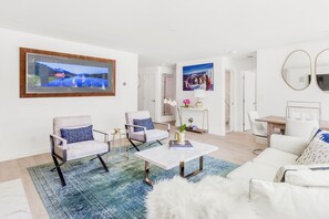 Una sala de estar moderna con un sofá blanco, dos sillones, una mesa de centro y un televisor montado en la pared.